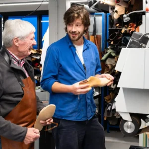 Schoenmaker in gesprek met bezoekers over ambacht en leerbewerking in het Schoenenlab.