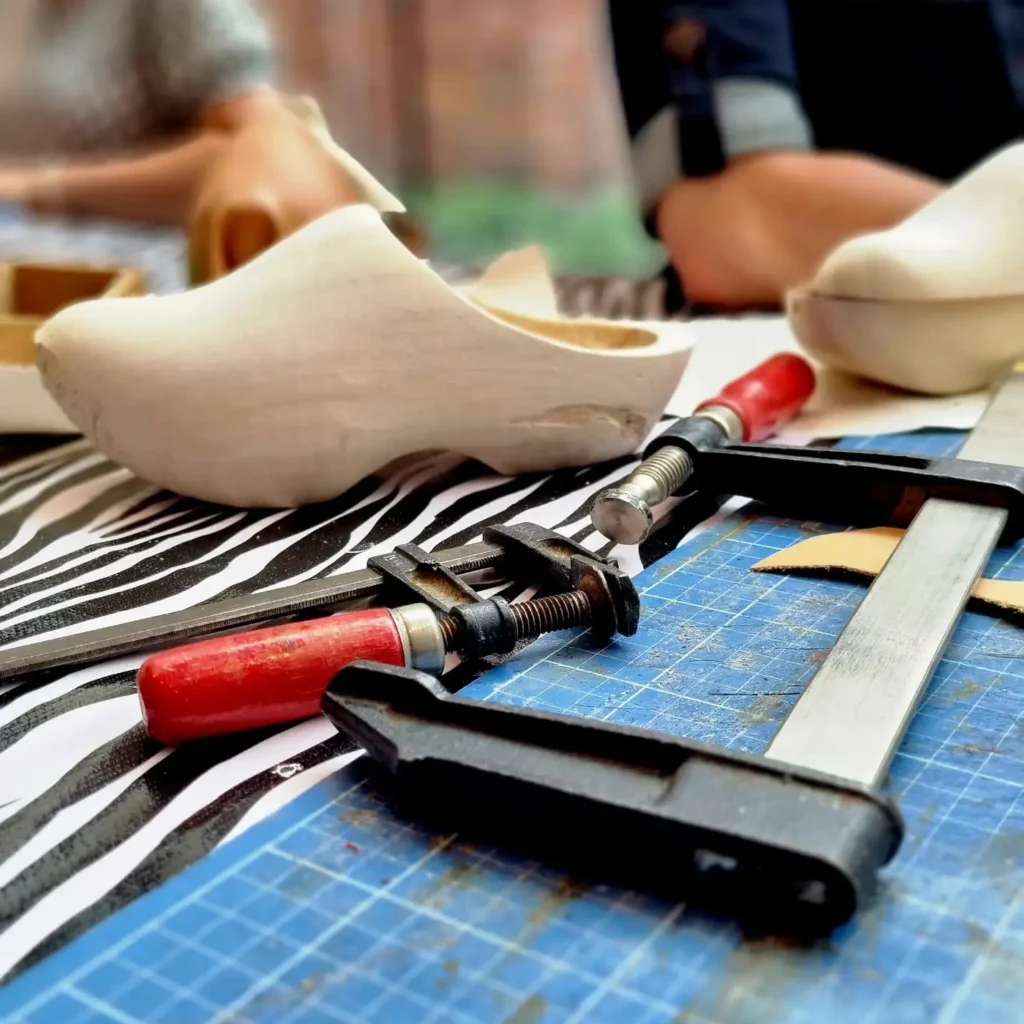 Schoenmaker werkt met gereedschap aan een klomp in het Schoenenlab.
