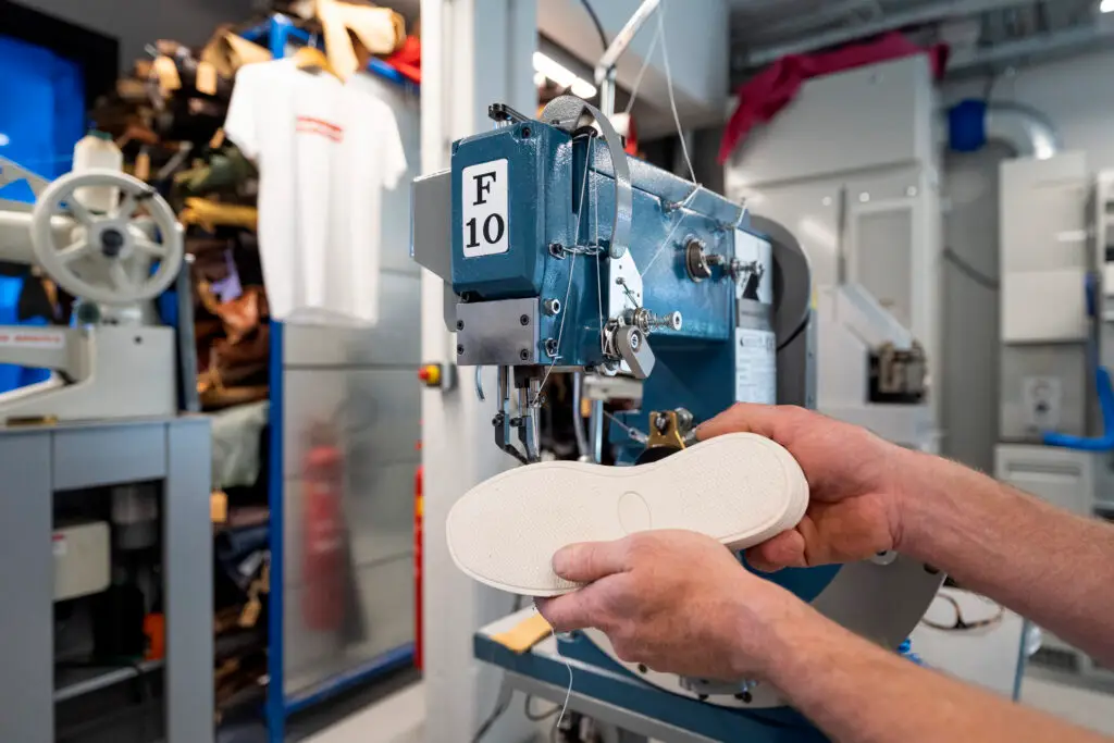 Maker attaching sole to shoe on a shoe sole stitching machine in the Shoe Lab.