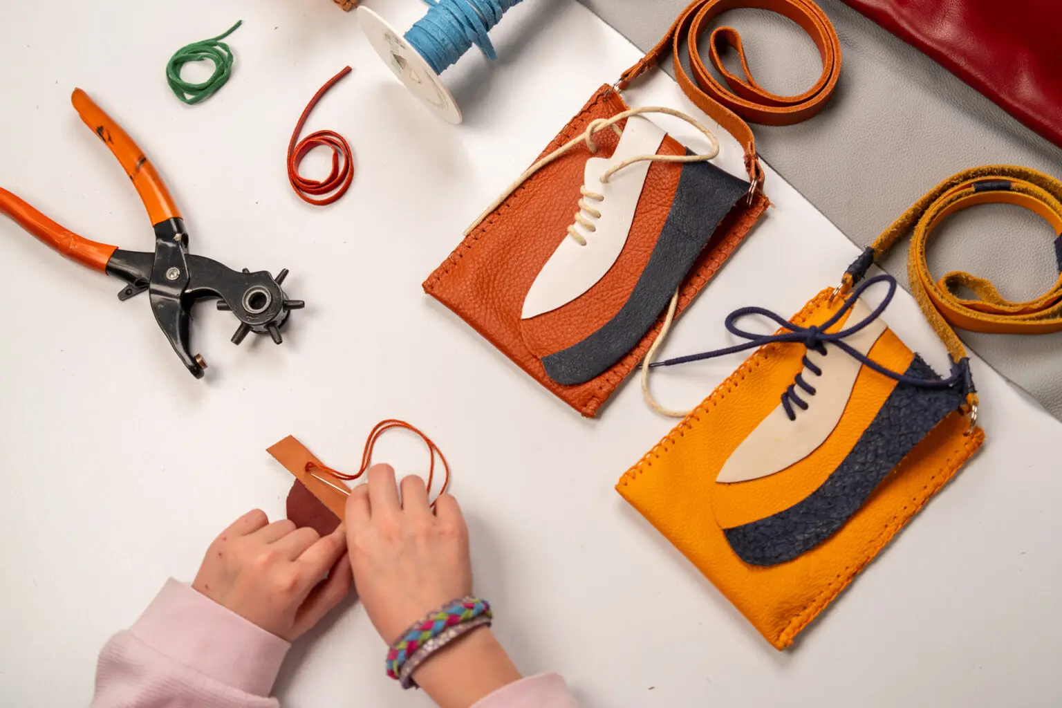 Werktafel met leren telefoontasjes, gereedschap en materialen tijdens een creatieve workshop in het Schoenenkwartier.