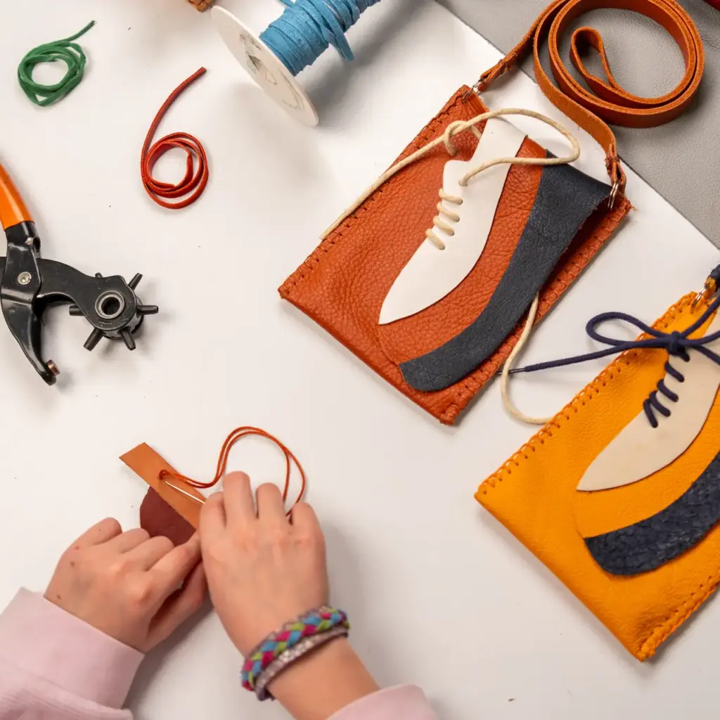 Werktafel met leren telefoontasjes, gereedschap en materialen tijdens een creatieve workshop in het Schoenenkwartier.
