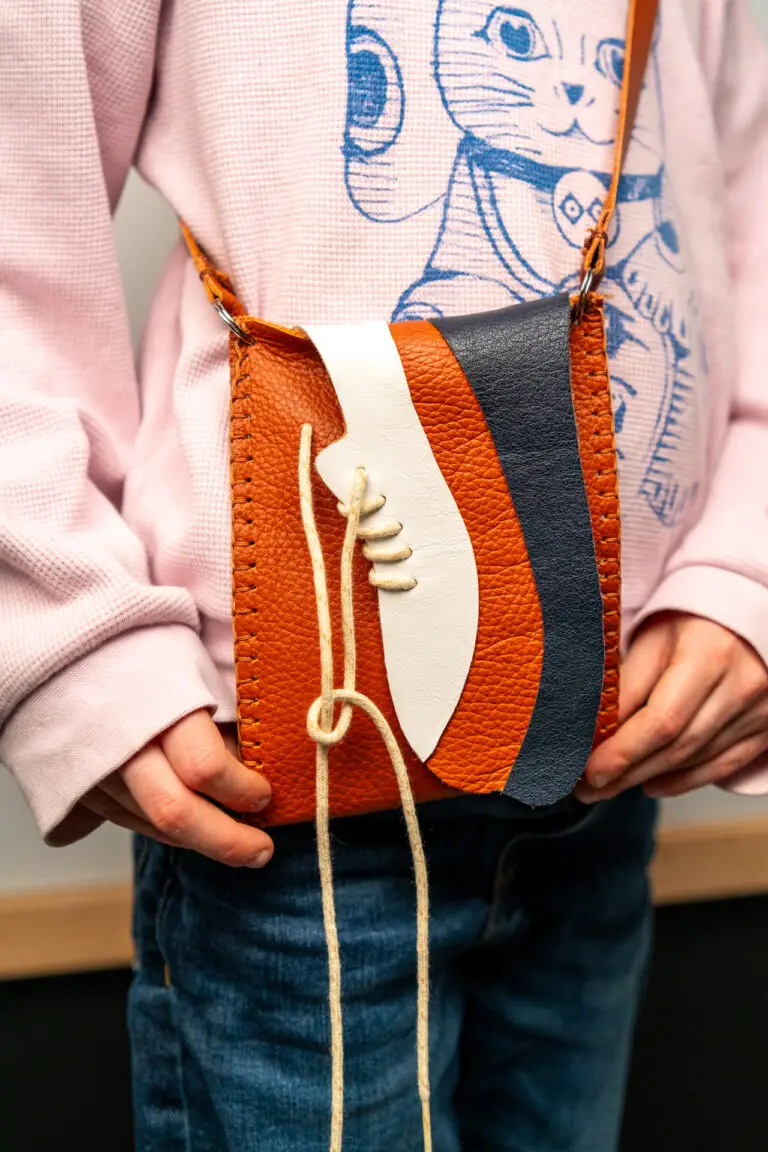 Kind draagt een zelfgemaakt leren telefoontasje tijdens een kinderworkshop in het Schoenenkwartier.