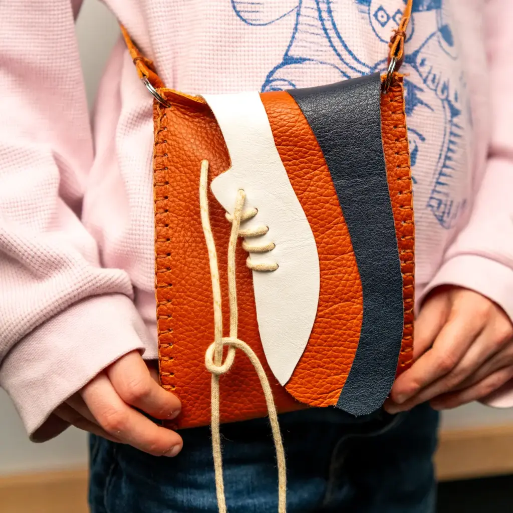 Kind draagt een zelfgemaakt leren telefoontasje tijdens een kinderworkshop in het Schoenenkwartier.