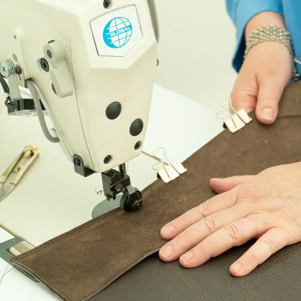 Handen begeleiden leer onder een naaimachine tijdens een workshop in het Schoenenlab van het Schoenenkwartier in Waalwijk.