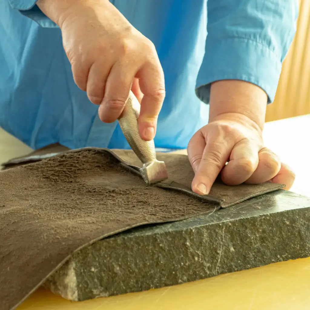 Handen snijden leer op een gele werktafel tijdens een workshop in het Schoenenlab van het Schoenenkwartier in Waalwijk.