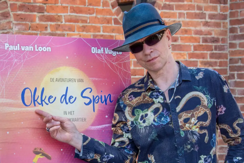 Paul van Loon naast de boekomslag van de avonturen van Okke de Spin in het Schoenenkwartier tijdens de boekpresentatie.