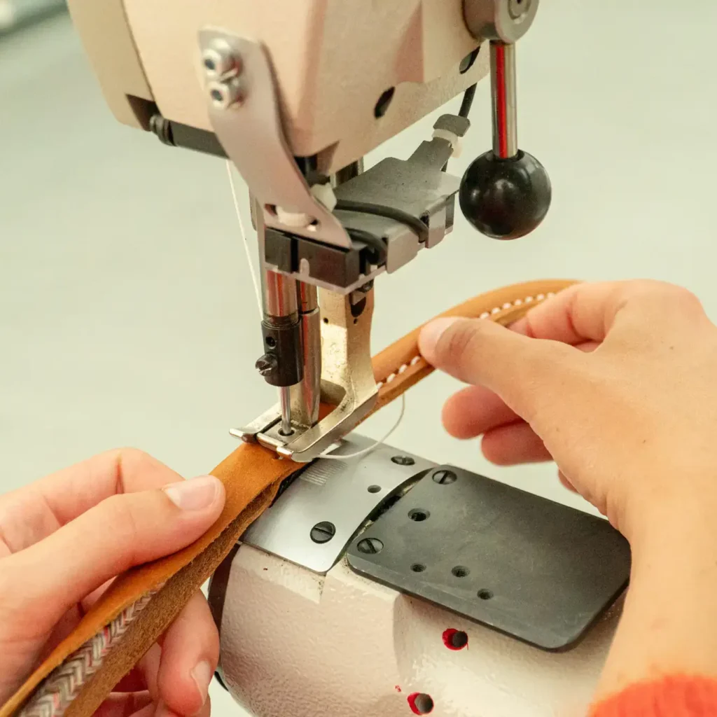 Detail van leer dat wordt gestikt op een industriële naaimachine tijdens schoenproductie.