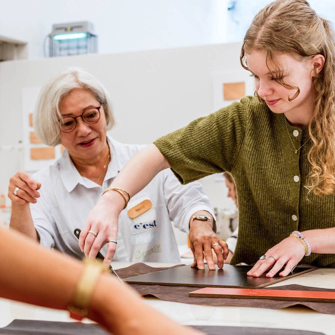 Een vrijwilliger begeleidt een deelnemer bij het werken met leer tijdens een workshop in het Schoenenlab van het Schoenenkwartier in Waalwijk.