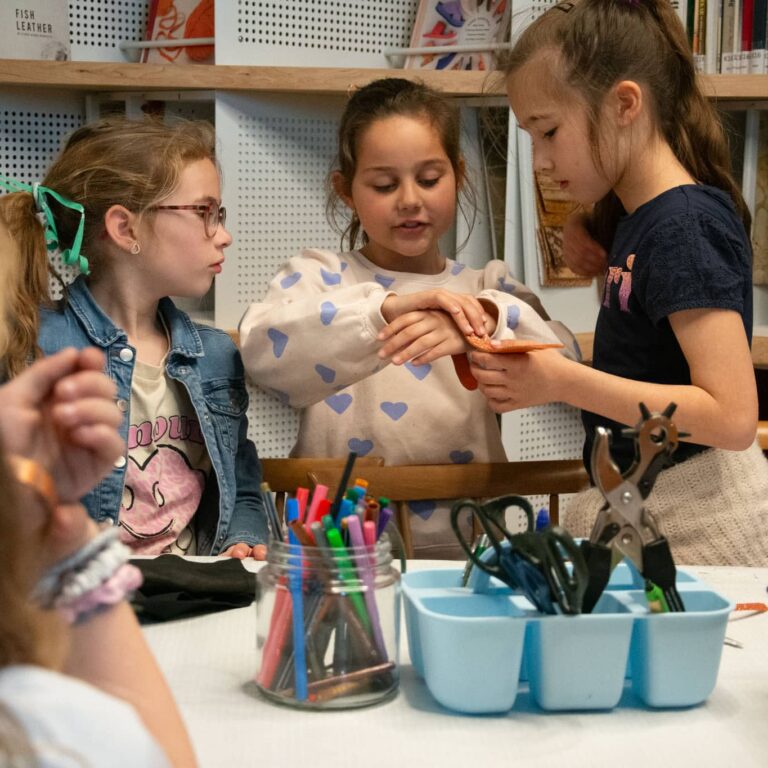 Kinderen knutselen met professionele gereedschap aan hun armbandje zien die ze maakten tijdens een workshop die werd gehouden tijdens het kinderfeest in het Schoenenkwartier