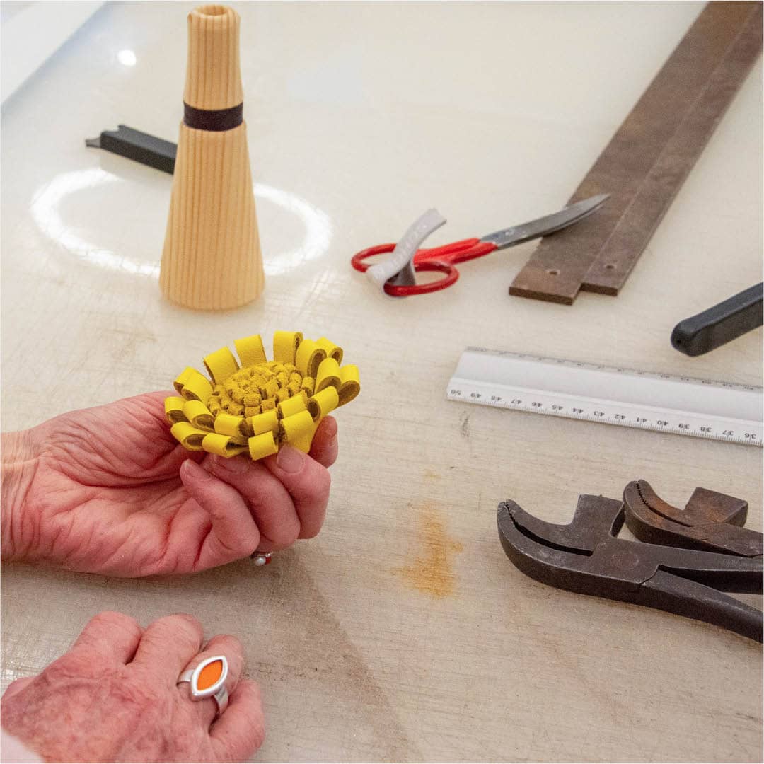 Handen werken met geel leer en gereedschap tijdens een leren bloemen maak workshop in het Schoenenkwartier.
