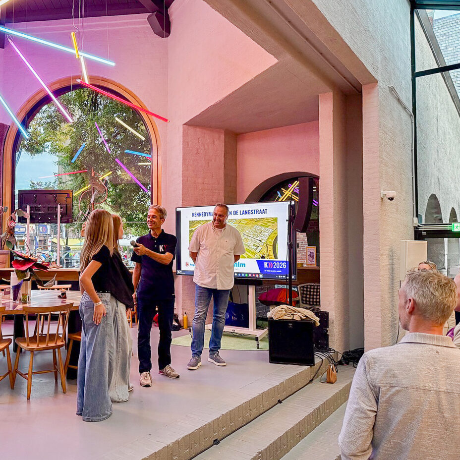 Een presentatie in de kiosk van het museumcafé, met een spreker voor een televisie scherm en een zittend publiek in het Schoenenkwartier in Waalwijk.