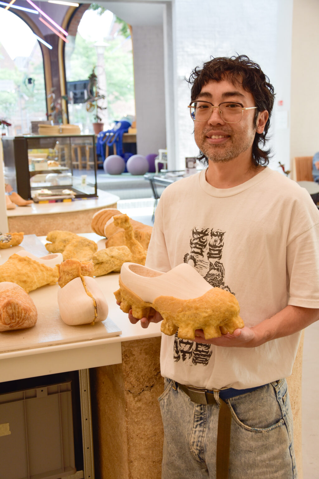 Portret van Wataru Sato in het Schoenenlab van het Schoenenkwartier in Waalwijk, omringd door zijn GOM-sculpturen van crêperubber en hout.