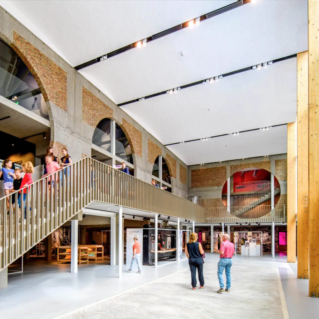 Atrium of the Shoe Quarter museum with large circular openings in the walls and visitors walking down the stairs and into the hall, Kropholler complex